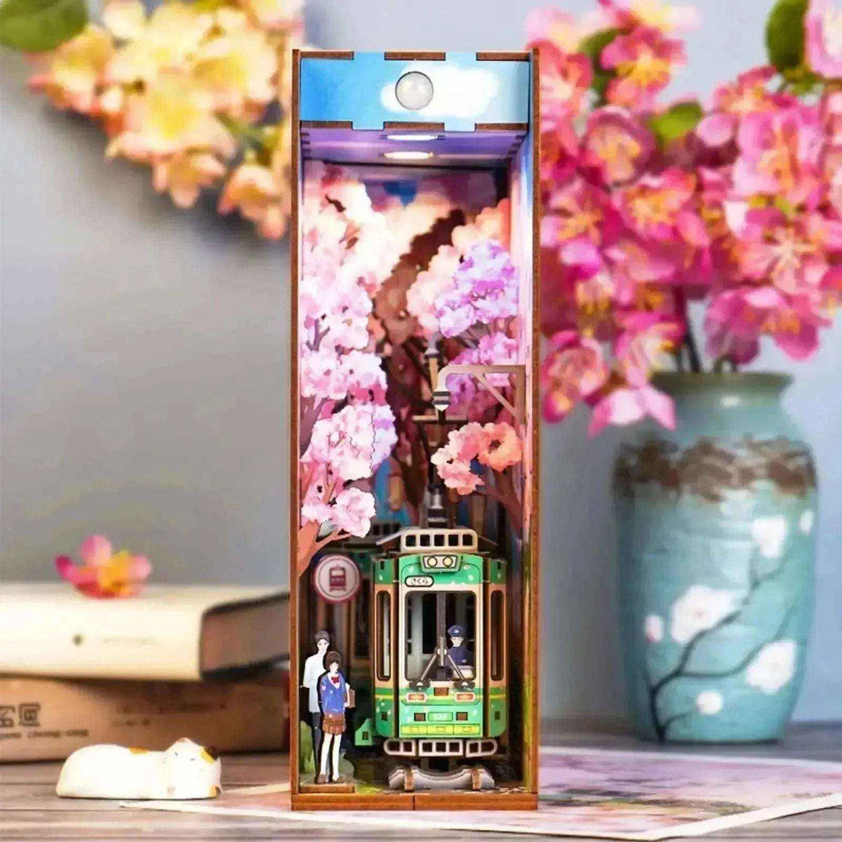 Sakura's Travel book nook with a green tram beneath pink cherry blossoms.