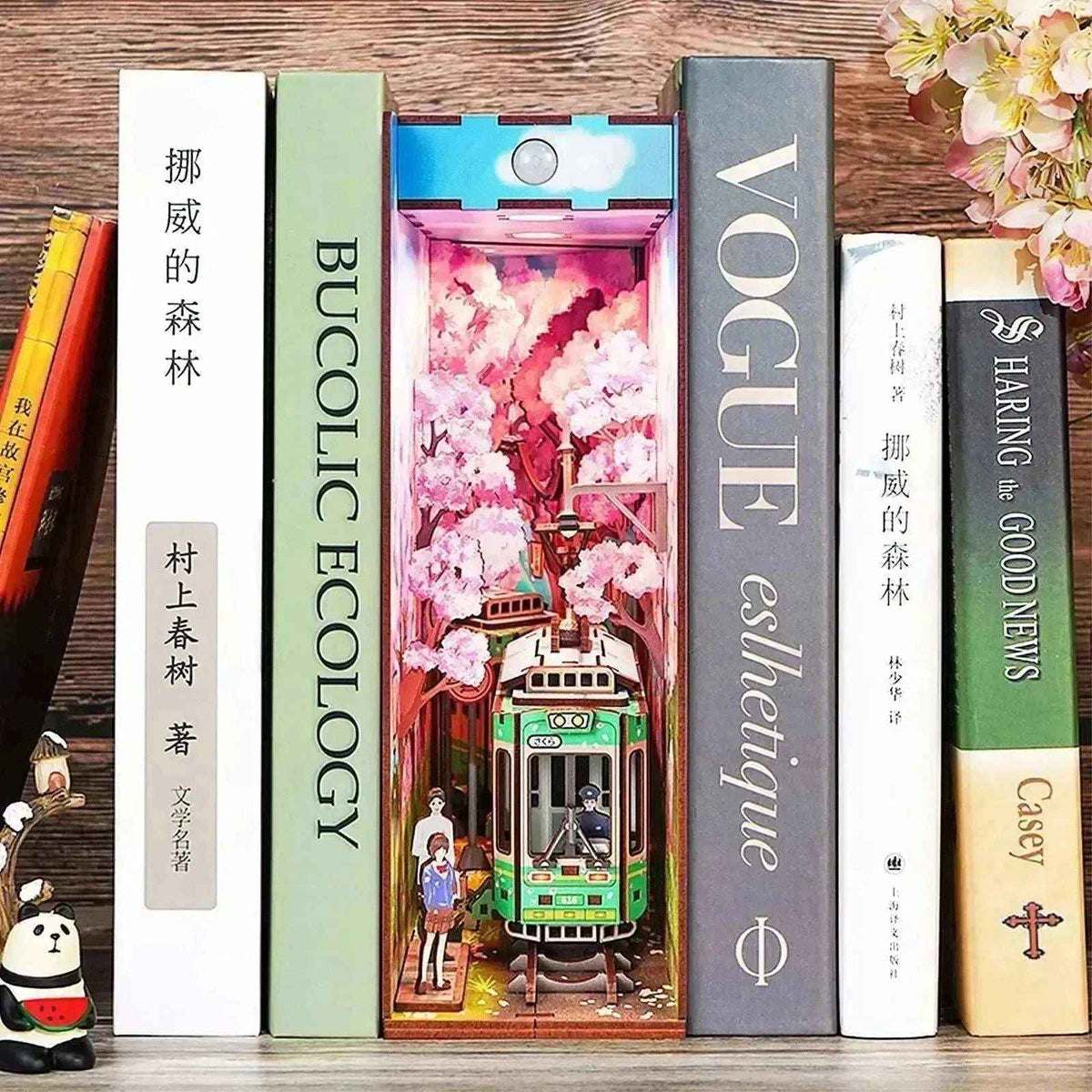 Sakura's Travel Japanese tram book nook displayed between books with a small panda ornament nearby.