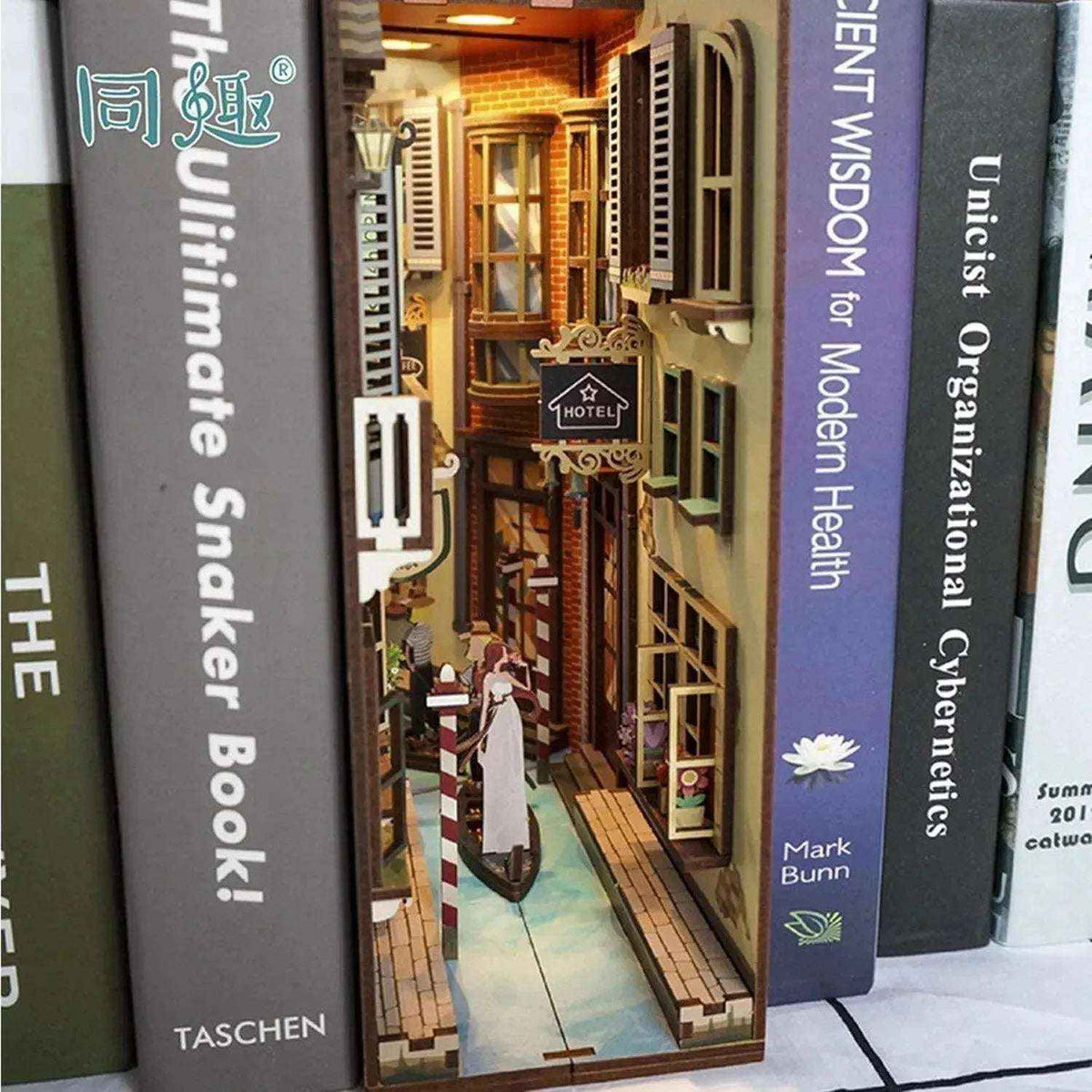 Angled Travel in Venice canal book nook between books, with miniature shop signs and a gondola.
