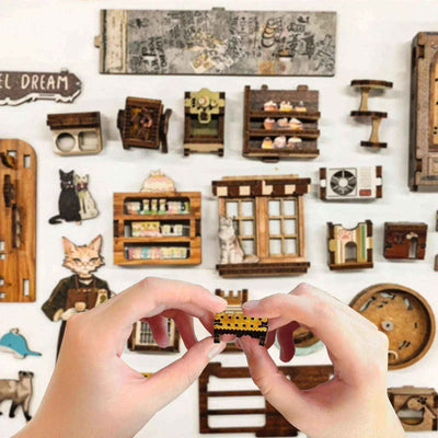 Hands assembling Caramel Dreams miniature parts beside coffee-shop accessories and cat-themed pieces.