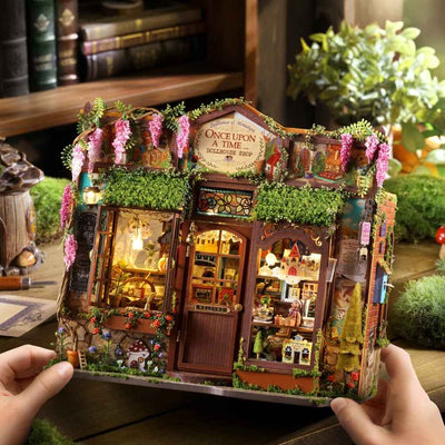 Hands holding Fairy-Tale Wonderhouse, a flower-covered miniature shop with warm-lit windows.