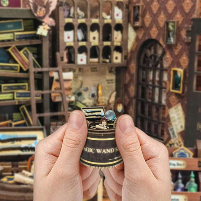 Hands holding a miniature cash register beside the Magic Wand Store interior.