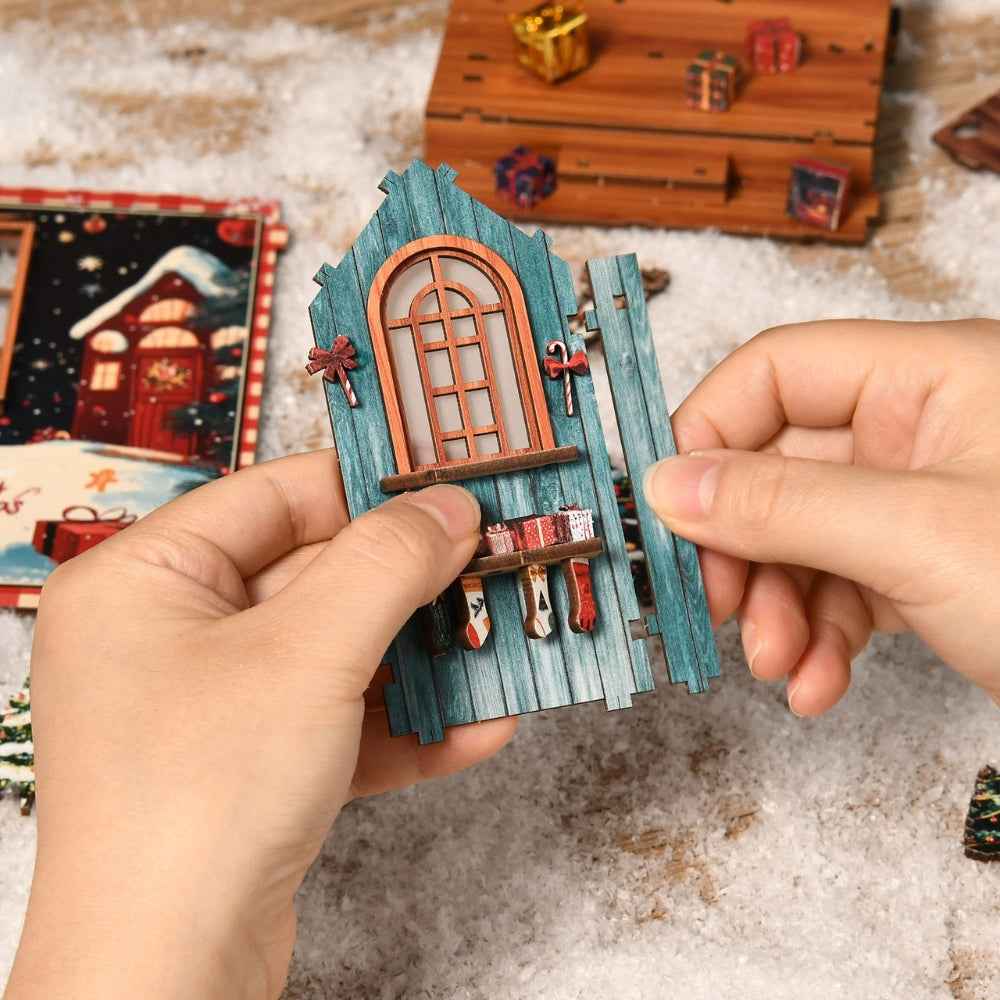 Hands assembling a blue window panel with miniature stockings for Snow Realm Wei Pavilion.