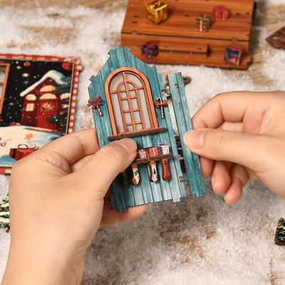 Hands assembling a blue window panel with miniature stockings for Snow Realm Wei Pavilion.
