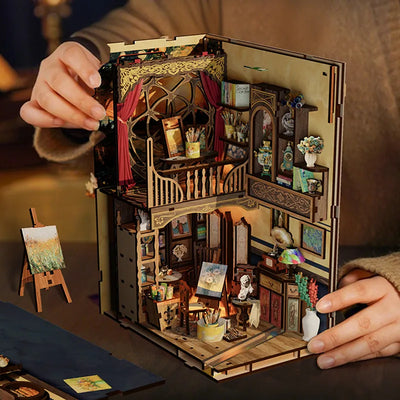Hands opening Whispers of Starlit Frames to reveal the miniature art studio and decorated panels.